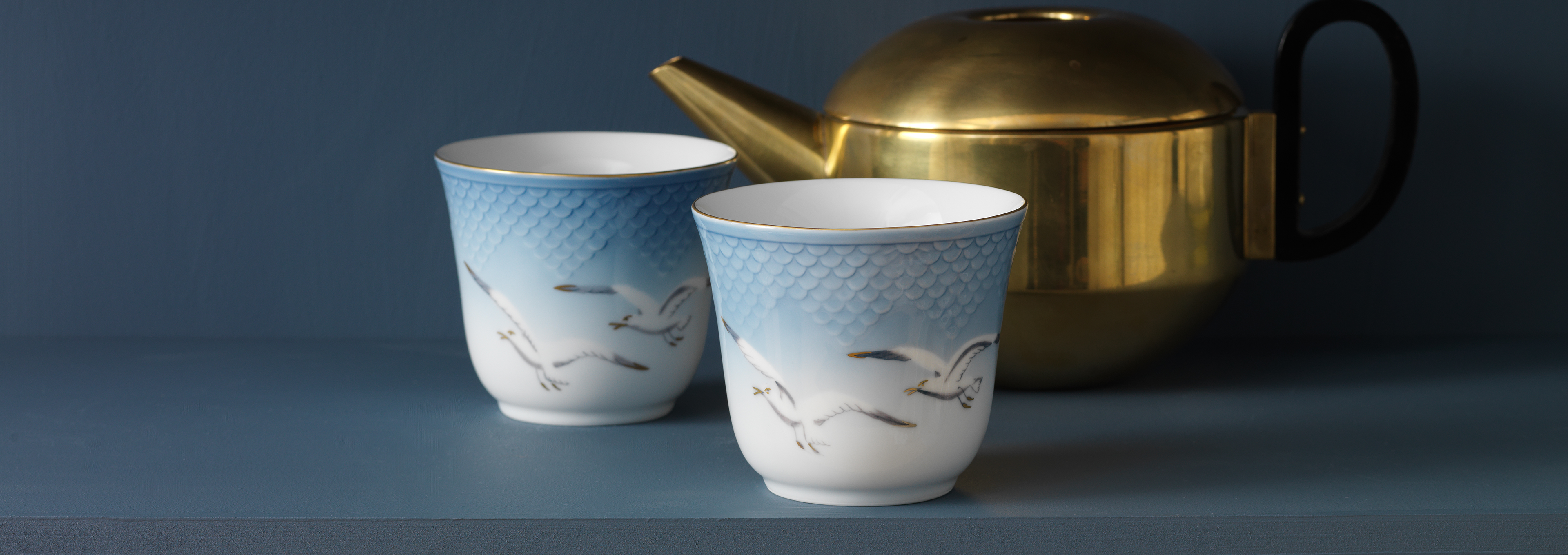 Two Seagull Thermal mugs standing on a table next to a golden teapot